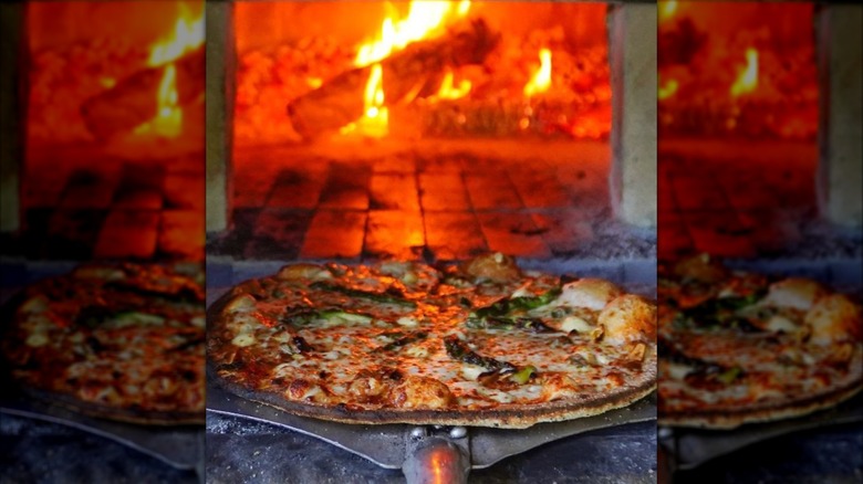 Pizza on a peel in front of blazing brick oven