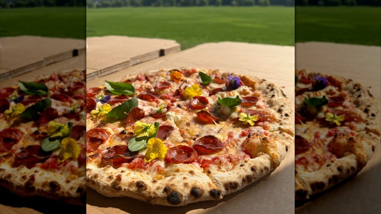 Pepperoni pizza with edible flowers on cardboard outside