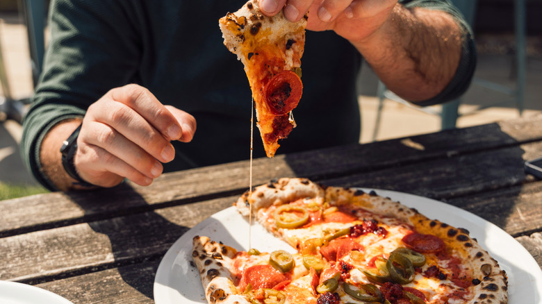 Person eating outside and reaching for a slice of wood-fired pepperoni pizza