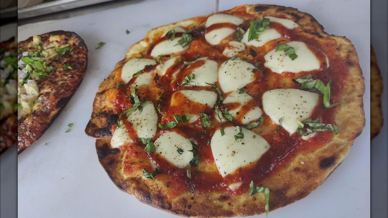 Wood-fired pizza with large pieces of mozzarella and shredded greens