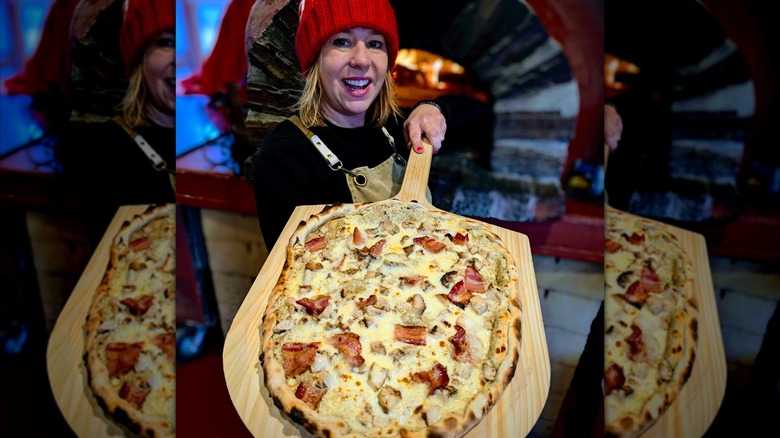 Smiling woman holding wood-fired pizza on a wooden board