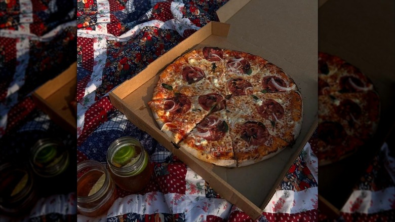 Pizza in an open box on a quilted picnic blanket