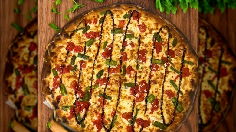 Pizza with cheese, veggies, and drizzle on a wooden table