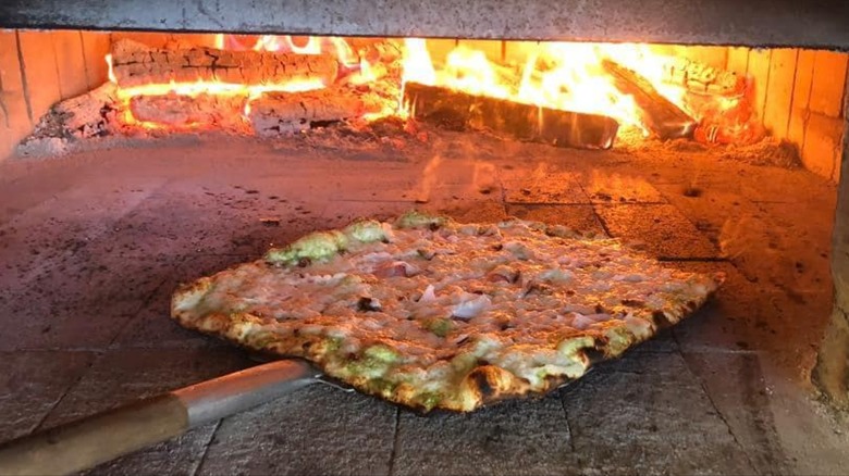 Pizza in a brick oven with wood fire in the back