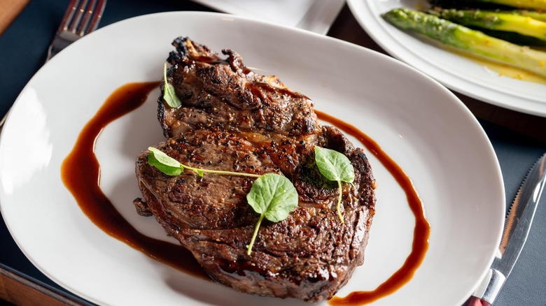 Bone-in ribeye on white plate with side of asparagus
