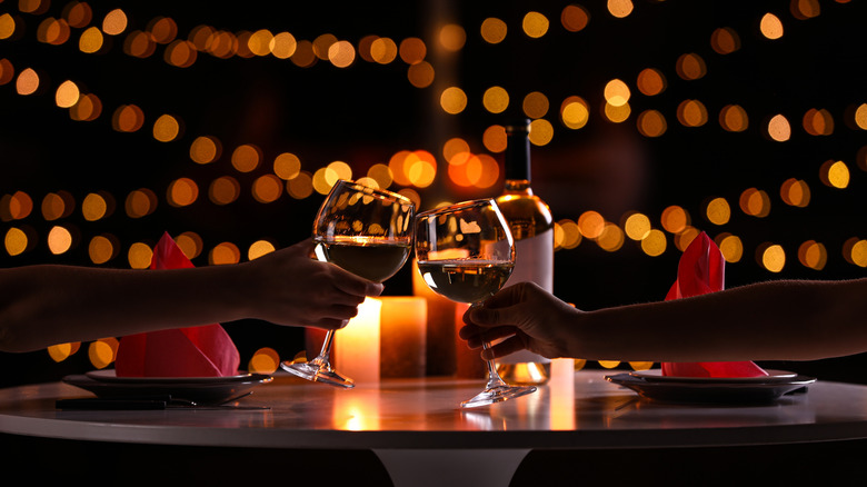 unidentified people clinking wine glasses over table with orange lights in background