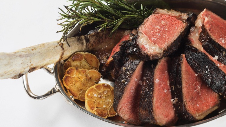 Silver dish with slices steak, rosemary, and toasted garlic on white background