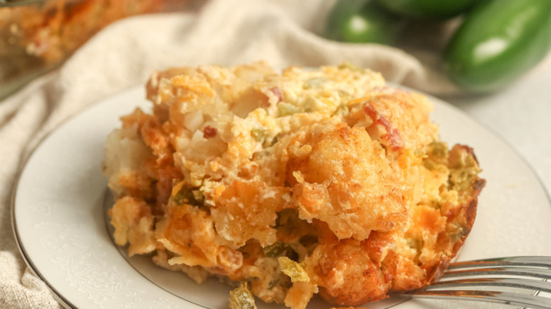 Fork digging into a slice of crispy jalapeño-topped tater tot casserole on a white plate