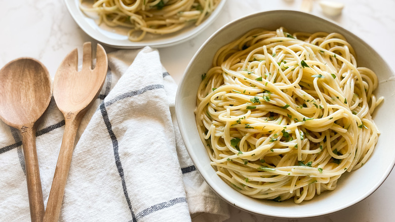 A bowl of garlic butter noodles beside napkin with serving utensils