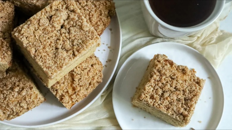 Squares of coffee cake on plate with single slice on small plate with coffee