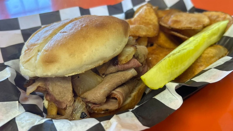 Sliced roast beef sandwich with chips and a pickle