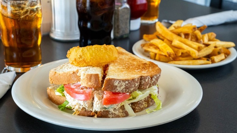 Sandwich with an onion ring and a plate of fries on a diner table