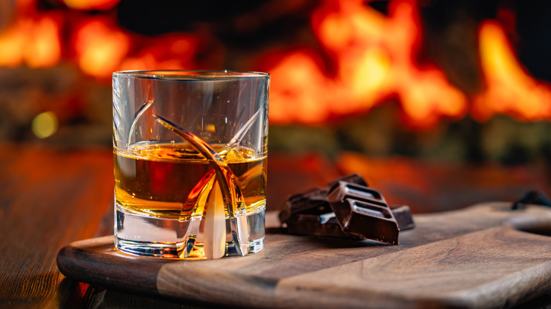 Glass of whiskey and chocolate on wood table with fire background