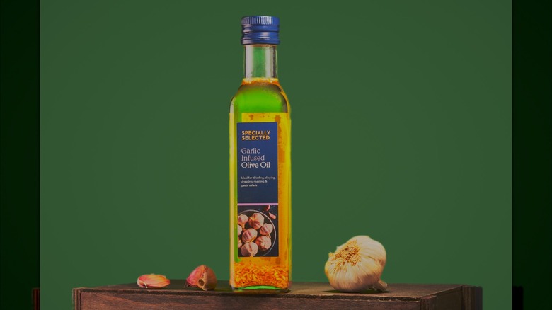 Bottle of Aldi's Specially Selected olive oil next to olives and garlic, against a green background