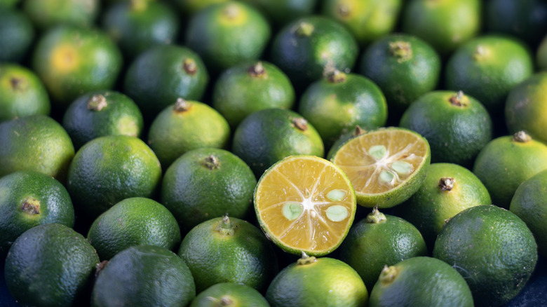 A large pile of whole calamansi with one cut in half showing orange flesh inside
