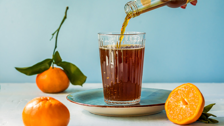 A glass of Chinotto being poured with the citrus of the same name surrounding