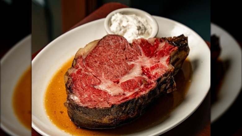 Slice of prime rib on plate with au jus and dish of horseradish