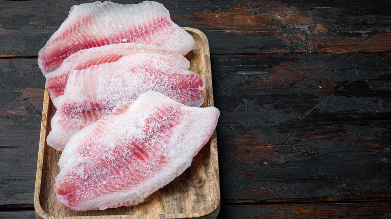 Raw frozen tilapia filets on wooden background