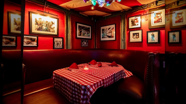 Leather booth with a red tablecloth against red walls with assorted photos at Chez Jay