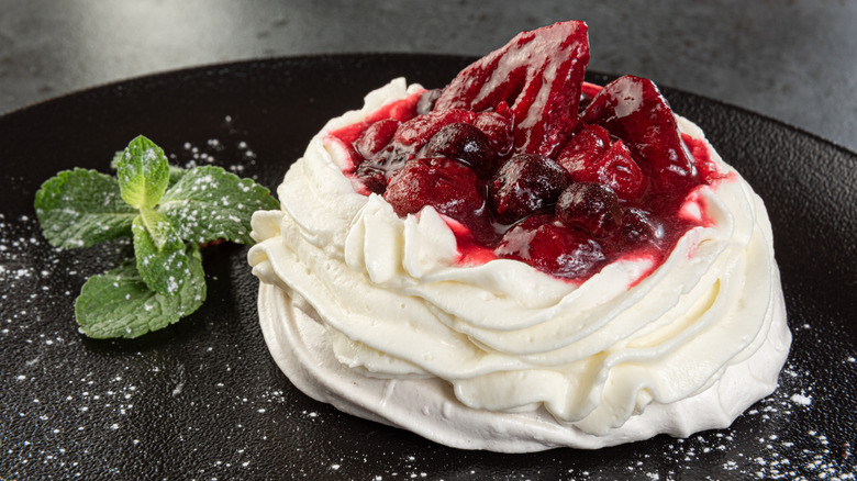 pavlova with cream, berries, and jam on black plate