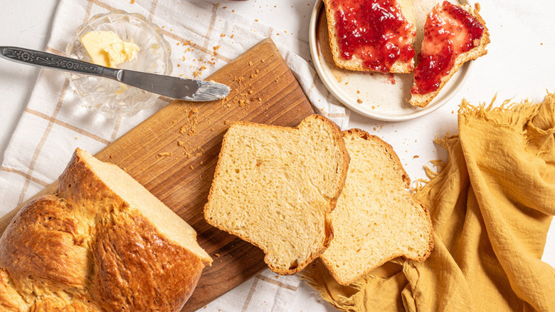 Sliced brioche bread on a wooden board, next to slices spread with jam on a plate