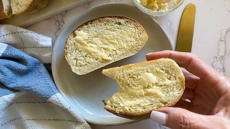 Hand lifting buttered, bitten slice of French bread from a white plate