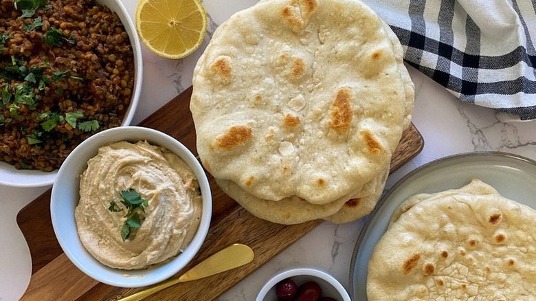 Pile of pita breads on a wooden board with a bowl of creamy dip