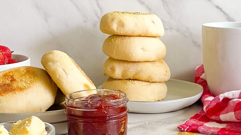 Stack of English muffins on a white plate next to a jar of strawberry jam