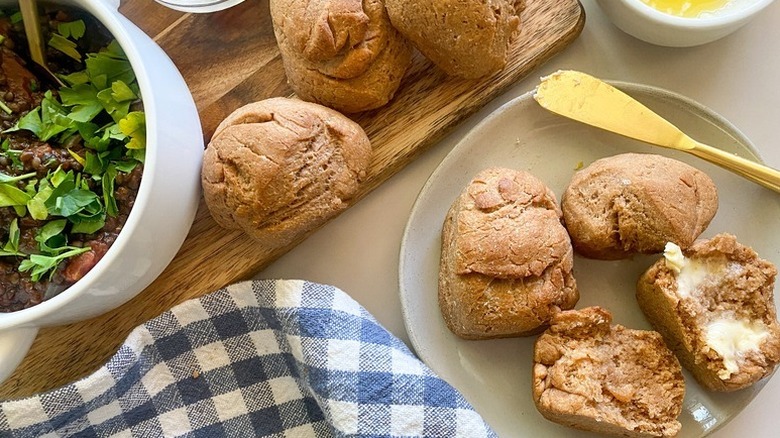 Whole wheat dinner rolls on a white plate and wooden board