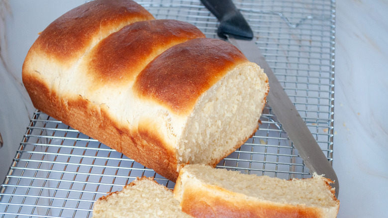 Sliced loaf of milk bread on a metal cooling rack with a knife