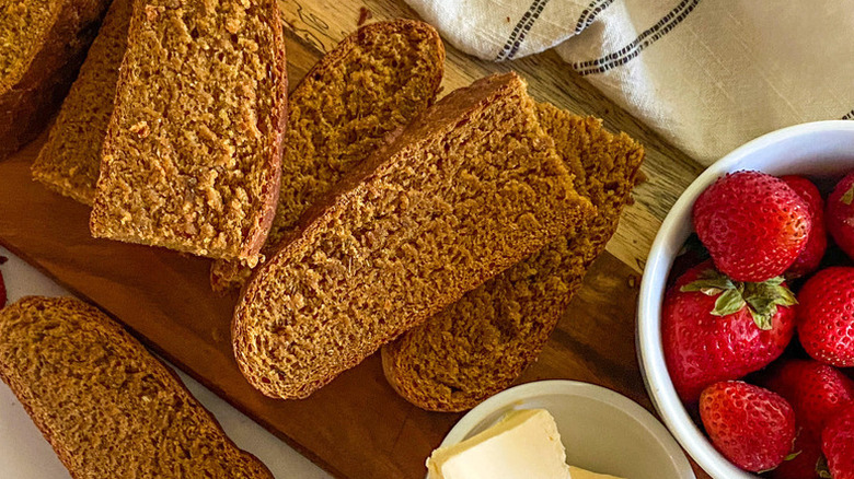 Slices of Swedish limpa bread on a wooden board with bowls of fresh strawberries and butter