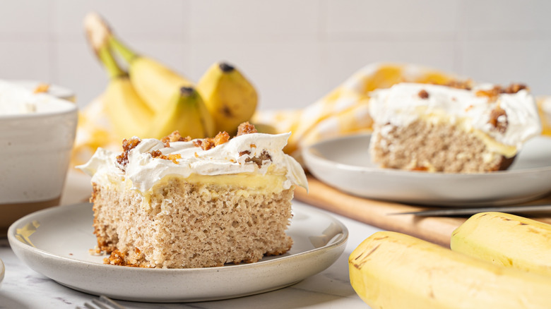 Two slices of banana pudding cake on plates surrounded by bananas