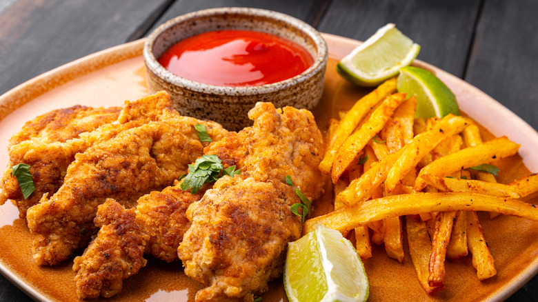 Plate of chicken tenders with french fries, lime wedges, and cup of red dipping sauce