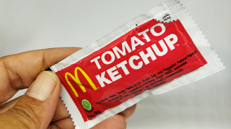 A hand holding a red and white McDonald's ketchup packet