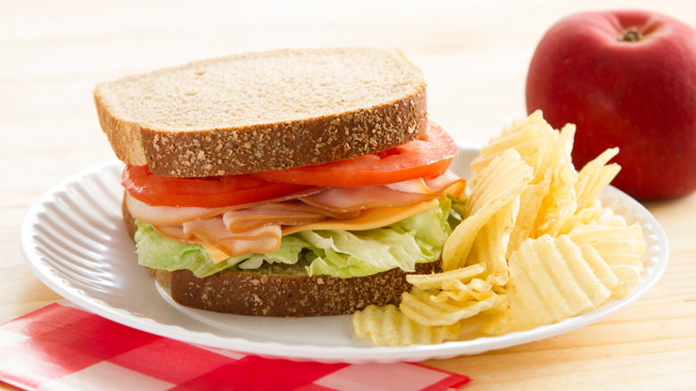 Turkey and cheese sandwich served with chips and an apple.