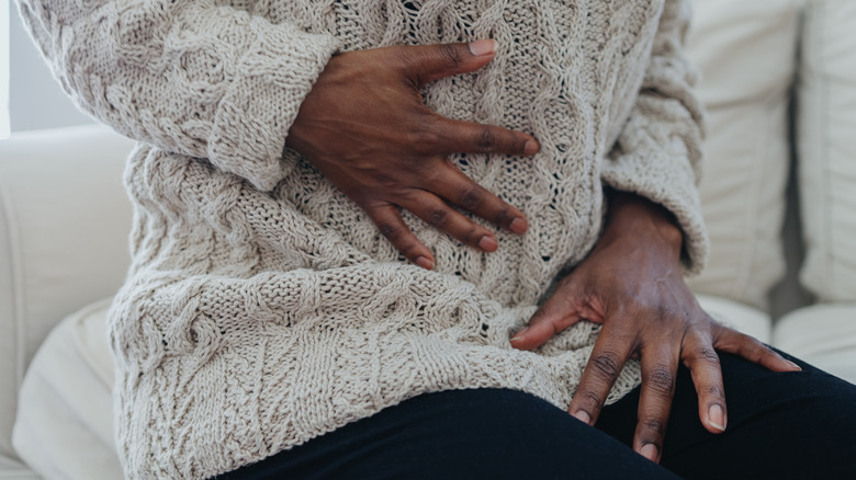 Person in a knit sweater holding their stomach in pain