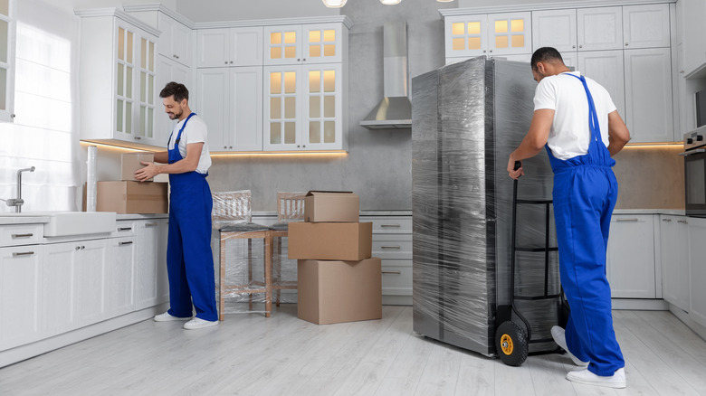 Two people moving a fridge into a new kitchen
