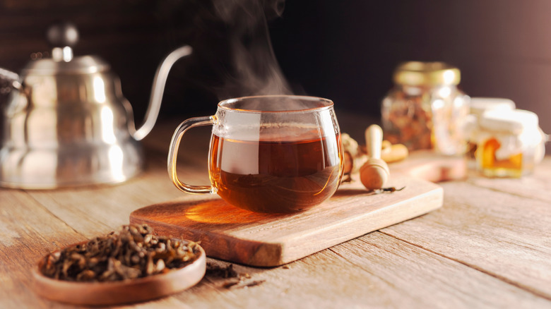 Dried leaves and tea with coffee pot or kettle in the background with a blurred pot of honey