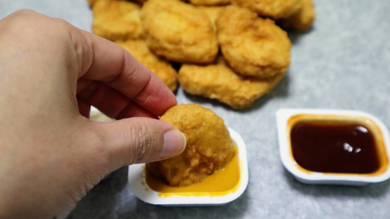 A person dipping chicken McNuggets in sauce