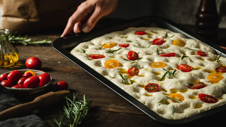 A person preparing a homemade focaccia pizza for the oven