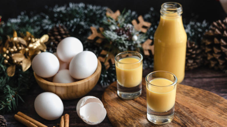 Jar and small glasses of eggnog with bowl of eggs.