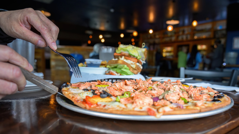 someone cutting up pizza at restaurant