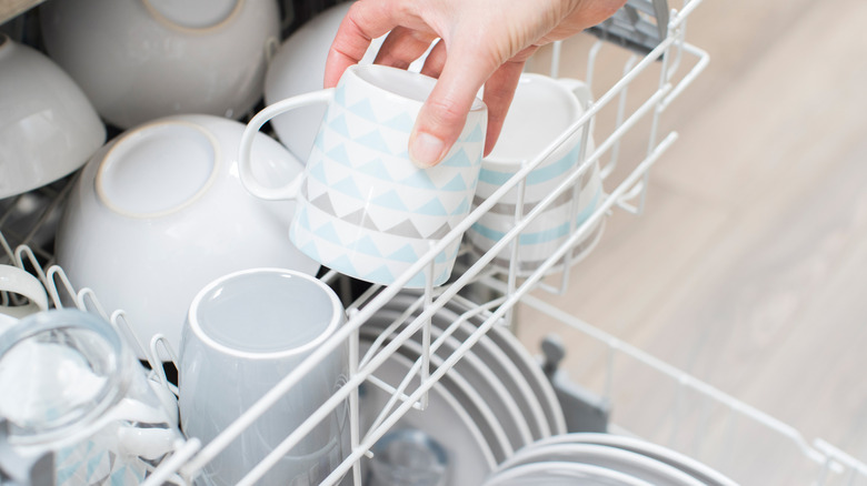 close up of woman's hand loading cups into dishwasher