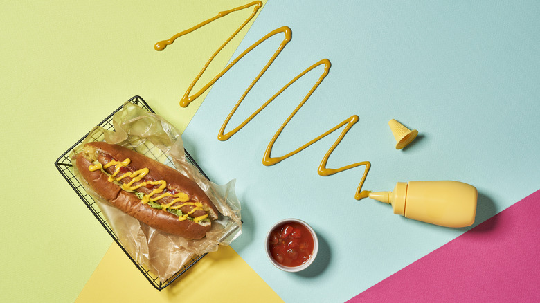 hot dog with mustard bottle drizzled on colorful background
