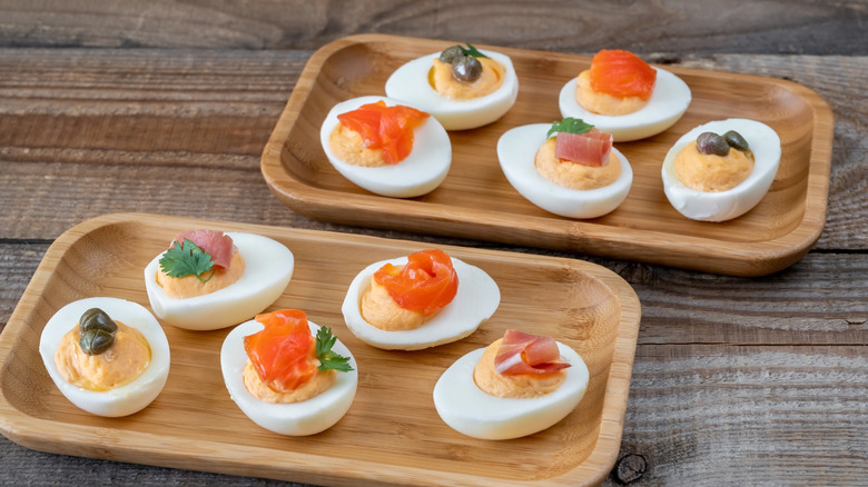 A plate of deviled eggs topped with different foods