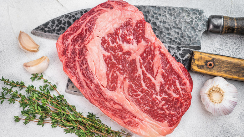 Ribeye cap with marbling along with garlic cloves and knives