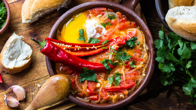 Dish with tomatoes, onions, egg, and peppers sitting on a wooden table