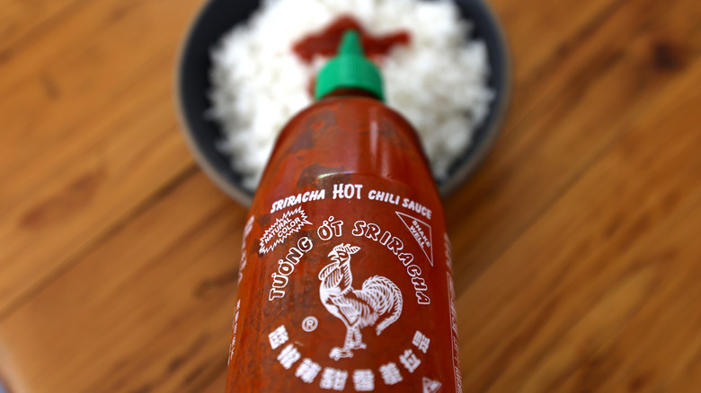 Bottle of Huy Fong Foods brand sriracha being squeezed over rice