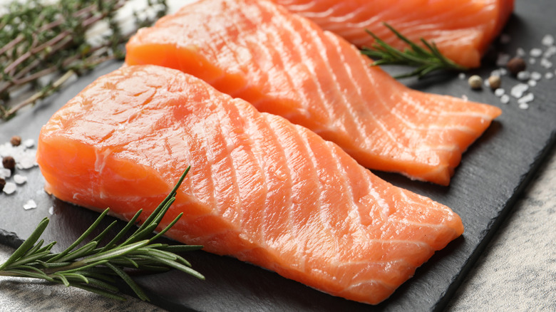 Raw salmon filets sit on a black slab