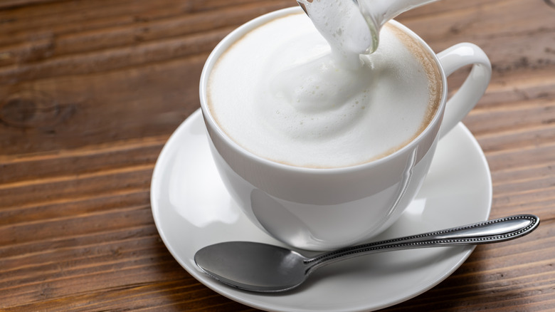 Overhead view of pouring frothed milk into a mug of coffee